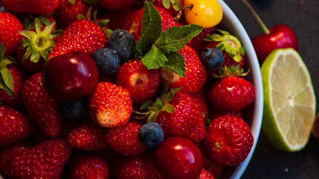 A colorful assortment of fresh strawberries, blueberries, cherries, and lime in a bowl, perfect for summer.
